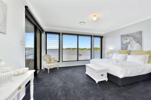 a bedroom with a large white bed and large windows at Water's Edge Apartment 2 absolute waterfront at Fishing Point on Lake Macquarie in Fishing Point