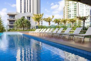 a row of white lounge chairs next to a swimming pool at ULTIQA Signature at Broadbeach in Gold Coast