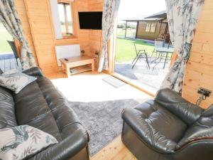 ein Wohnzimmer mit Ledercouch und Fernseher in der Unterkunft Ty Will, Parc Y Fronwen in Newborough