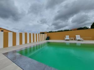 - une piscine avec 2 chaises blanches à côté d'un bâtiment dans l'établissement O Cantinho do Sol (Estúdio Chocolate), à Lourinhã