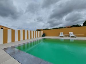 a swimming pool with two white chairs next to a building at Cantinho do Sol (Estúdio Prata) in Lourinhã