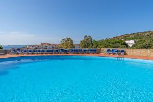 a large swimming pool with blue chairs and the ocean at Baja di Li Ranci by DomusAway in Baja Sardinia