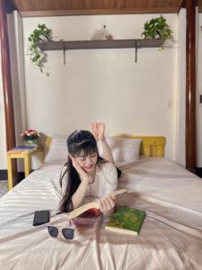 Una joven acostada en una cama leyendo un libro en Homestay San Hô, en Dong Hoi