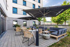 eine Terrasse mit Tischen, Stühlen und einem Sonnenschirm in der Unterkunft Premier Inn Heidelberg City Bahnstadt in Heidelberg