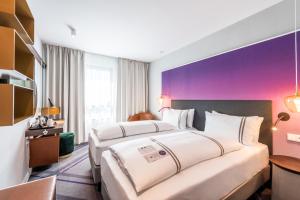 two beds in a hotel room with a purple wall at Premier Inn Heidelberg City Bahnstadt in Heidelberg