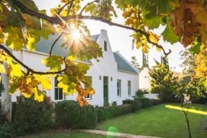 a white house with the sun shining through trees at Huckleberry House - La Bruyere Farm in Tulbagh