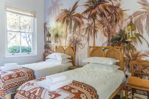 two beds in a room with palm trees on the wall at Huckleberry House - La Bruyere Farm in Tulbagh