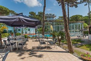 un patio con mesas, sillas y una sombrilla en Hotel Meridianus, en Lignano Sabbiadoro