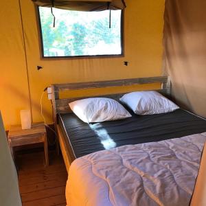 1 cama con 2 almohadas en una habitación con ventana en Camping Le Mondou en Saint-Julien-de-Lampon