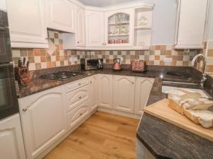 a kitchen with white cabinets and a black counter top at Sunshine Cottage Tideswell, Games room included. in Tideswell