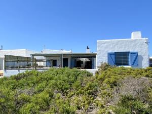 una casa blanca con una ventana azul y arbustos en Beach House en Paternoster