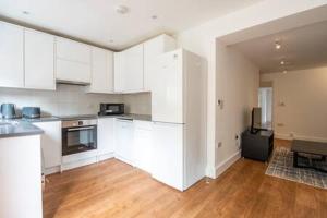 a kitchen with white cabinets and a wooden floor at London Flat with Garden WPRA in London