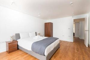 a white bedroom with a large bed and a wooden floor at London Flat with Garden WPRA in London