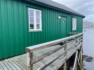 Kræmmervika Rorbuer - Rustic Cabins in Lofoten في بولستاد: مبنى أخضر مع سطح خشبي بجانب الماء