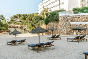 AluaSoul Mallorca Resort - Adults only في كالا ذاور: مجموعة من الكراسي والمظلات على الشاطئ