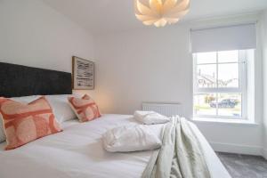 a white bed with orange and white pillows and a window at The Winnoch - modern 2 bed flat in Lochwinnoch