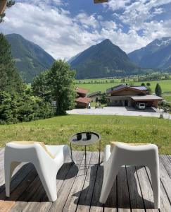 two white chairs and a table on a deck with mountains at Chalet Descansa in Neukirchen am Großvenediger
