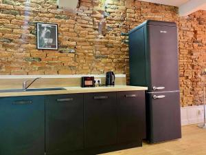 a kitchen with a black refrigerator and a brick wall at Le Passage de la Comédie - Climatisation & WiFi Fibre in Montauban