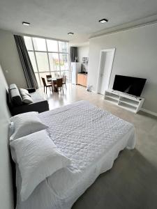 - une chambre avec un lit blanc et un salon dans l'établissement Studio Residencial no coração do 4° Distrito, à Porto Alegre
