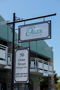 Dos carteles delante de un edificio con un cartel de una tienda. en Osler Place Self-Catering, en Stilbaai