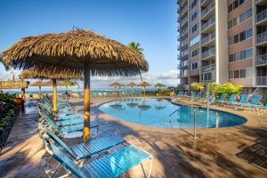 a swimming pool with chairs and a straw umbrella at Deluxe Oceanview Maui Studio..New & Updated in Kahana