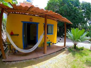 a small yellow house with a hammock on a deck at Residencial Caetanos - 5 casas em Arraial D'ajuda in Porto Seguro
