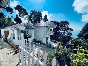 a white house with a white fence and flowers at Peky's in Kurseong