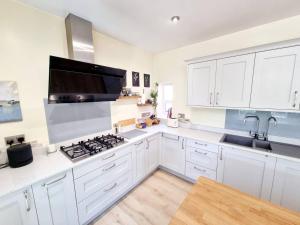 a kitchen with white cabinets and a stove top oven at Cosy Family Haven: Spacious 3-Bedroom Retreat in Christchurch in Iford
