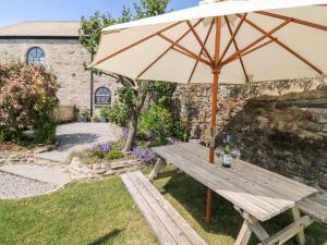 a wooden picnic table with an umbrella in a yard at Small Barn in Liskeard