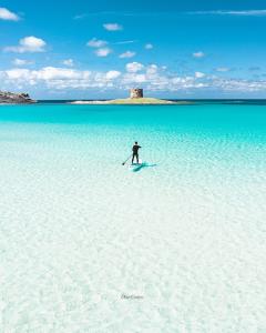 a person standing on a paddle board in the water at Ancóramare in Stintino