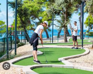 a woman is playing golf on a putting green at Apartman Punta Radman in Petrcane