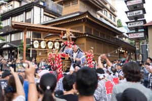 a parade with a man walking through a crowd of people at Tanuki Nozawa in Nozawa Onsen