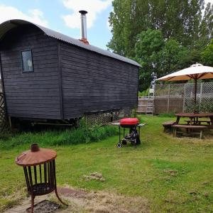 a black shed with a picnic table and a red stool at Lower Haven Shepherds Hut in Bath