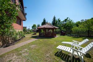 two white benches sitting in a yard with a gazebo at Domki, pokoje u Małgosi in Sztutowo