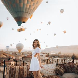 a girl in a white dress standing on a couch with hot air balloons at Zara Cave Hotel in Goreme