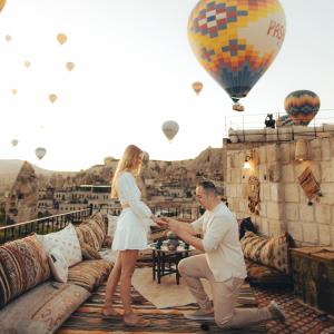 a man and woman standing on a balcony with a hot air balloon at Zara Cave Hotel in Goreme