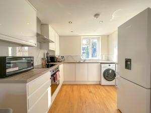 cocina con armarios blancos, lavadora y secadora en Parkway residences, en Londres