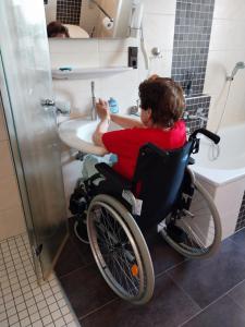 une femme en fauteuil roulant assise devant un lavabo dans une salle de bain dans l'établissement Rollstuhlgerechte 80m² grosse Ferienwohnung in Ostfriesland, à Utarp 27 autres photos