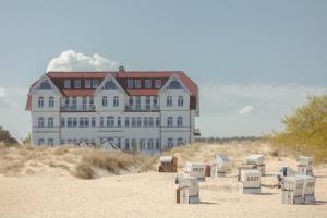 un grand bâtiment sur la plage avec des chaises dans le sable dans l'établissement Strandhotel Ostende, à Ahlbeck