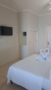 Cama blanca en habitación con TV en la pared en Hotel Pousada Miami, en Itanhaém