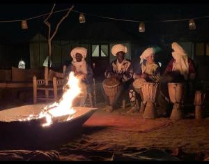 a group of people sitting around a fire at night at Morocco tours camp in Merzouga