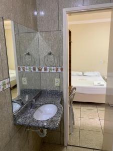 baño con lavabo, espejo y cama en Pissin Plaza Hotel, en Goiânia