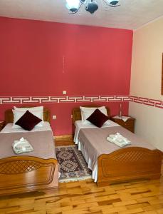 two beds in a room with a red wall at Christina's house with 2 bedrooms and free parking in Gjirokastër