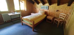 ein kleines Schlafzimmer mit einem Bett und einem Stuhl in der Unterkunft B&B Pension Lärch in Obergesteln