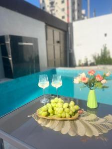 a table with two wine glasses and a plate of fruit at Uma Quadra do MAR Com PISCINA, Churrasqueira, 2 Vg de Garagem e 3 Quartos!!! in Praia Grande