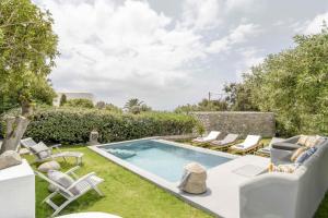 Villa Valente in Mykonos with two pools! في بلاتيس يالوس ميكونوس: حديقة خلفية بها مسبح وكراسي وساحة بها ساحة