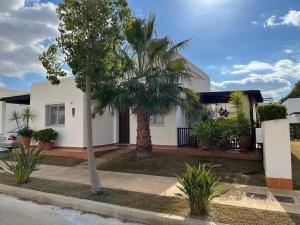 a white house with a palm tree in front of it at Casa la Vida - Golf villa with private pool in Alhama de Murcia