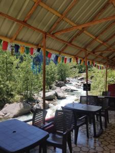 un patio con mesas y sillas junto a un río en Last Stop Riverside wooden Huts, Camps & Dorms en Manāli