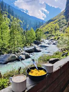 a bowl of food on a ledge next to a river at Last Stop Riverside wooden Huts, Camps & Dorms in Manāli
