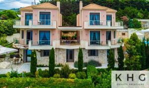 a large pink building with trees in front of it at Elli's Villas complex in Petani beach! Majestic wide angle sea views along Petani beach! in Vóvikes